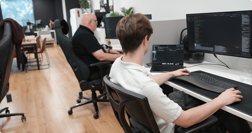two paladine systems developers working side by side at multi-monitor workstations with code open across their screens in the click click media norwest office.