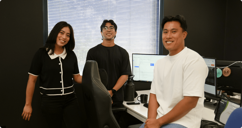 three click click media ppc specialists at a white desk reviewing the openai ads manager dashboard on a laptop alongside a google ads campaign overview on a second screen in the norwest office.
