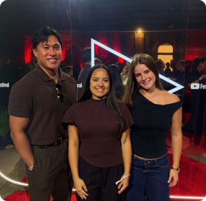 Three Click Click Media team members smile together at the YouTube Festival, under red event lighting.