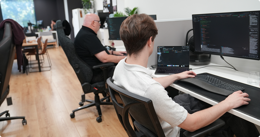 two paladine systems developers working side by side at multi-monitor workstations with code open across their screens in the click click media norwest office.
